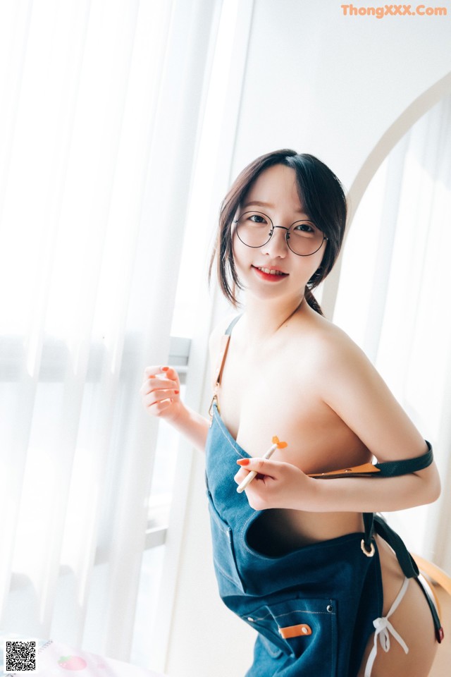 A woman wearing glasses and overalls posing for a picture.