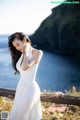 A woman in a white dress leaning against a wooden fence.