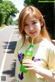 A woman holding a bottle of green juice on the side of a road.