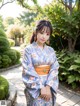 A woman in a blue kimono standing in a garden.