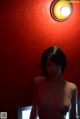 A naked woman standing in front of a red wall.