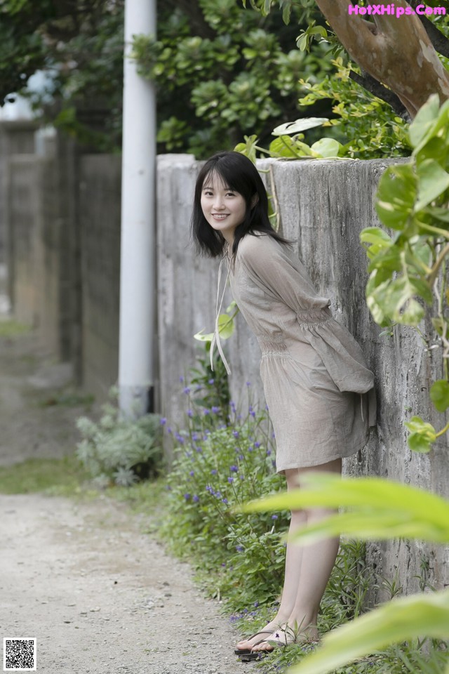 A woman leaning against a wall in a garden.