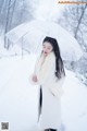 A woman standing in the snow holding an umbrella.