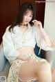 A woman sitting on a chair wearing a white shirt and skirt.