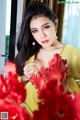 A woman in a yellow dress holding a bunch of red flowers.